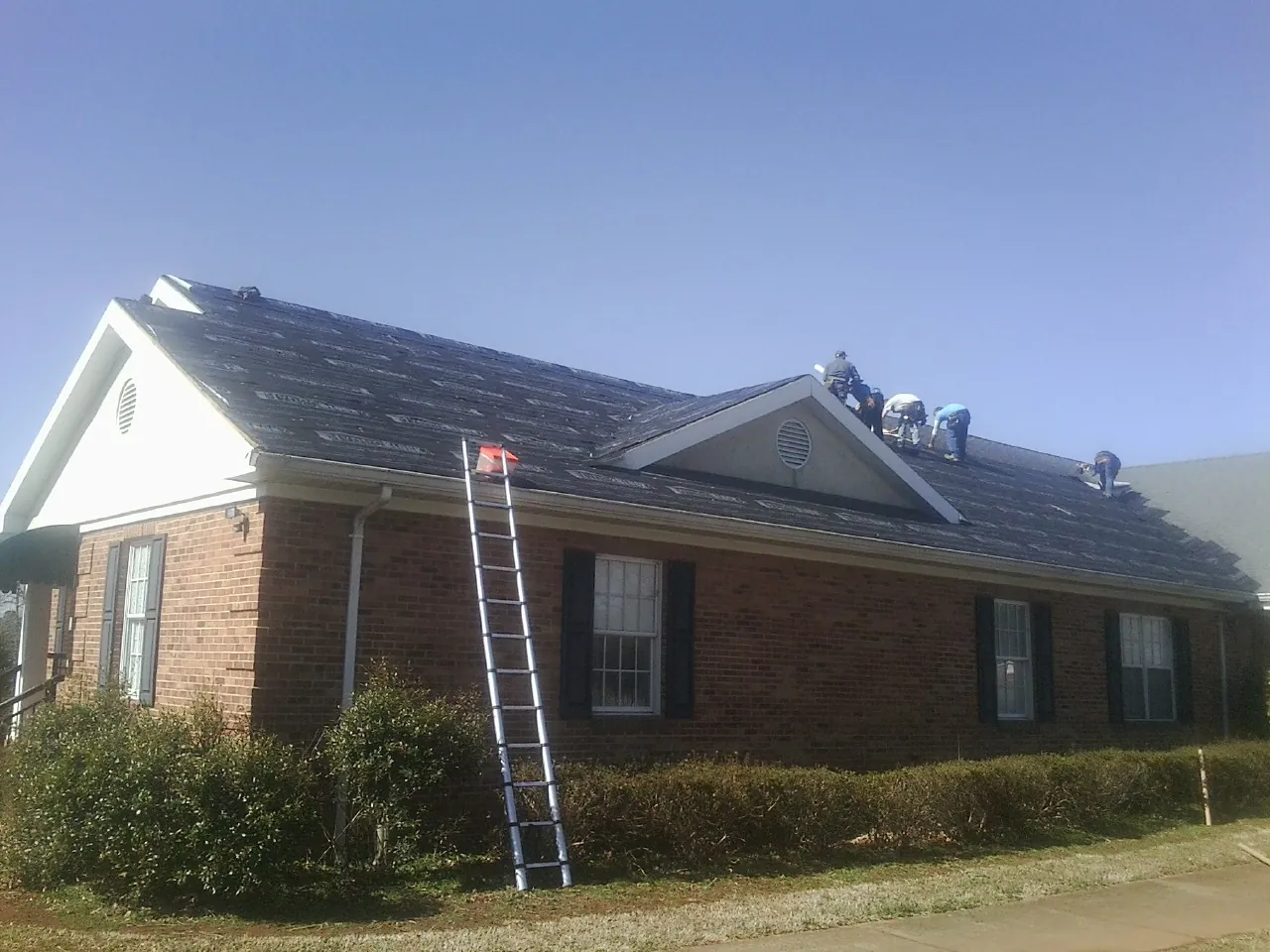 Crew tearing shingles off a brick ranch roof with a ladder set — Emergency Roof Repair work by our crew in Bowling Green