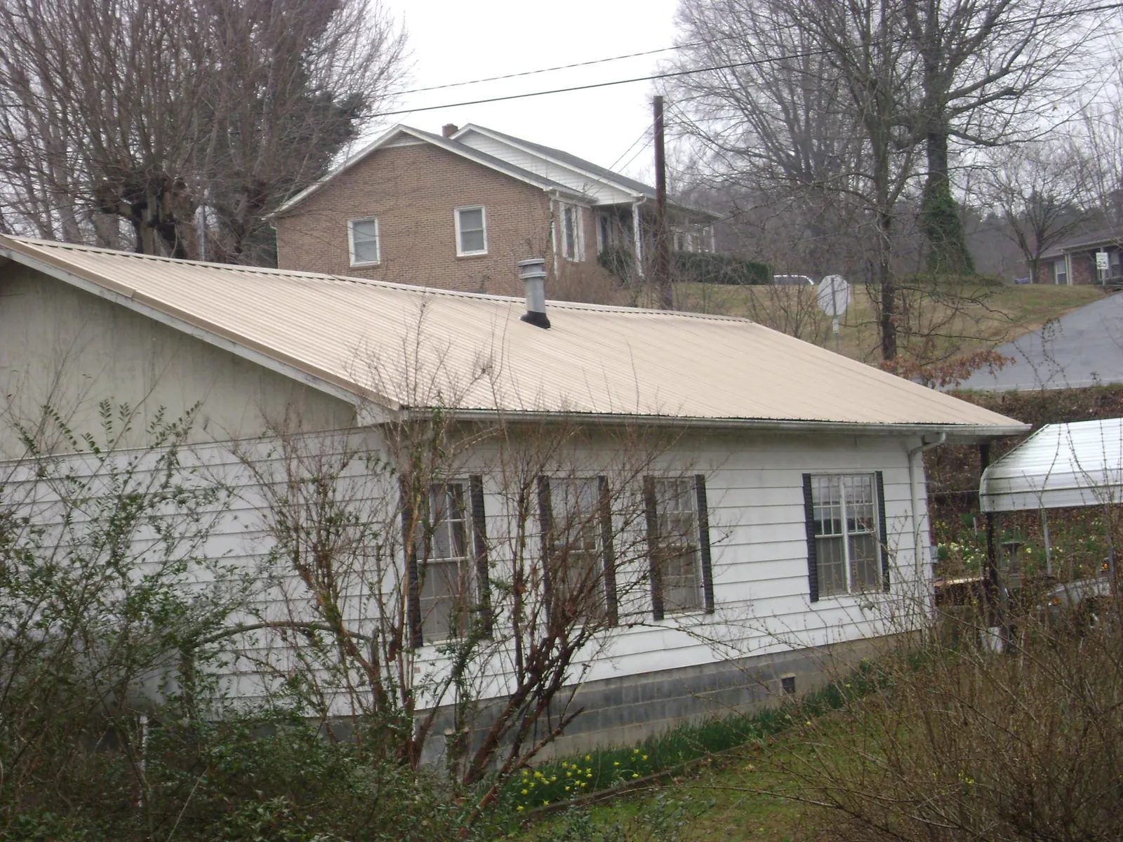 Tan metal roof on a white sided house set into a hillside — Commercial Roofing by Roofing Brothers in Bowling Green